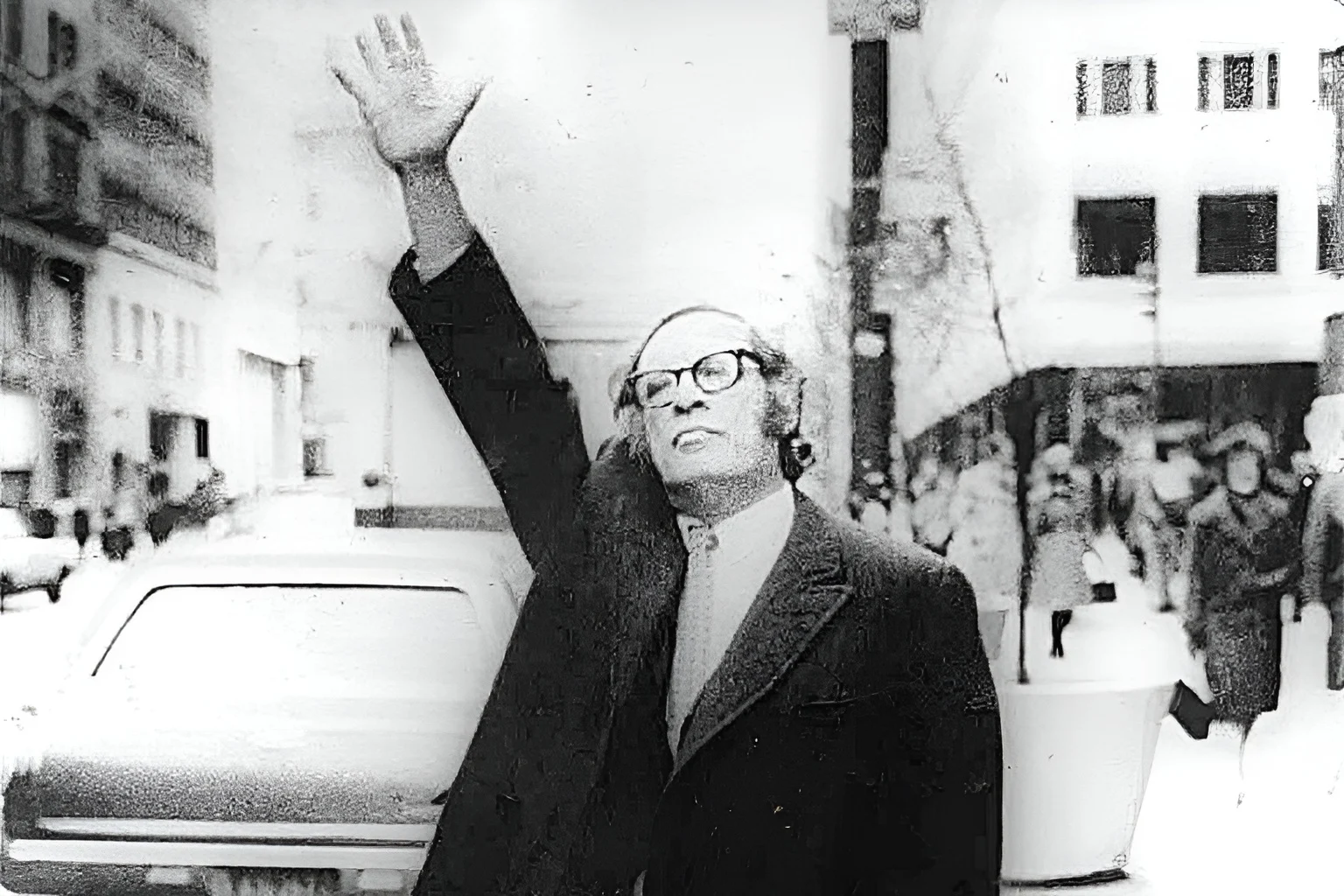 A imagem mostra o escritor Isaac Asimov em preto e branco, levantando a mão em um ambiente urbano, com pessoas e carros ao fundo. No contexto da discussão sobre globalismo e era espacial, a presença de Asimov reforça a reflexão sobre como a exploração espacial ampliou a percepção da humanidade como uma única entidade global.