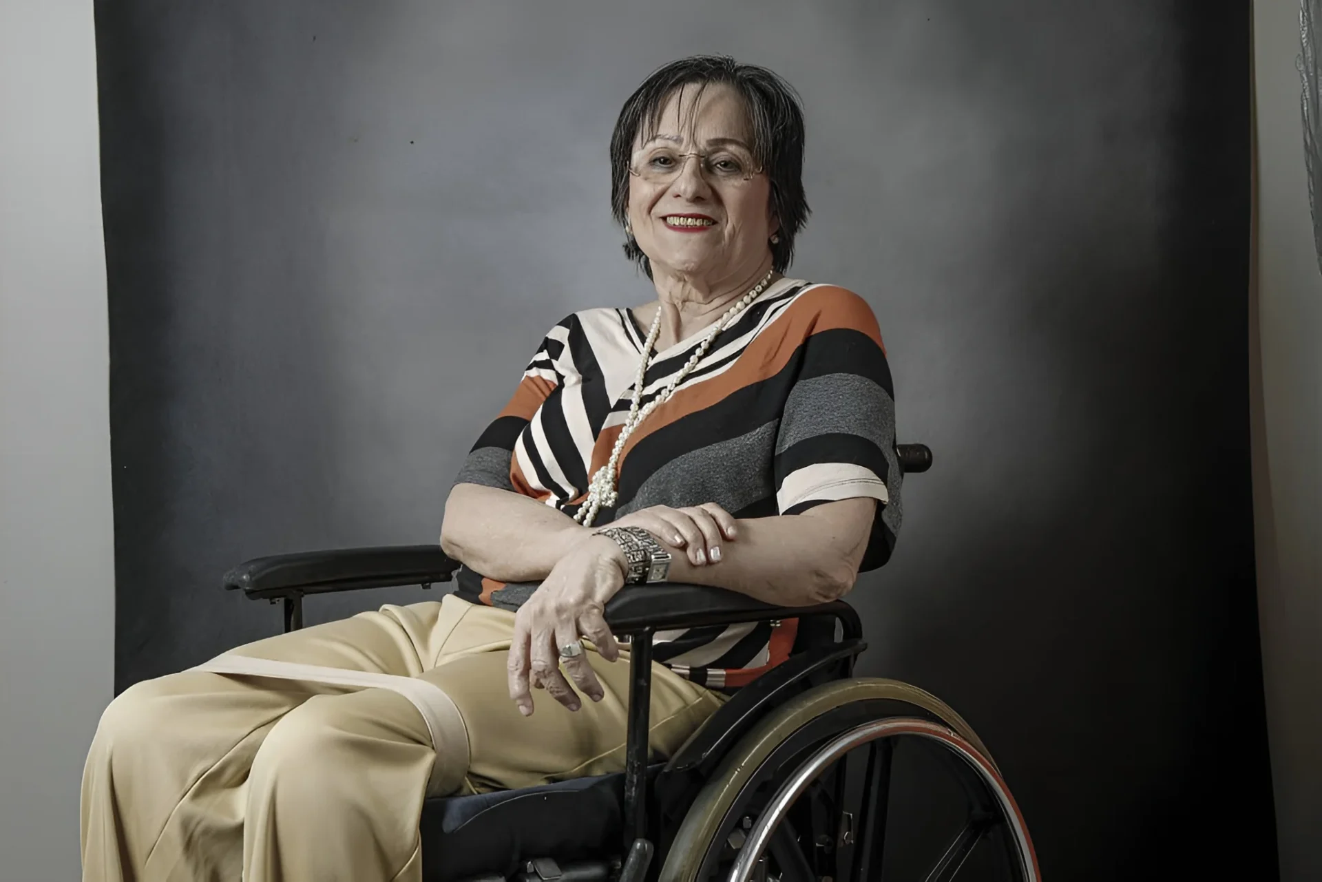 Maria da Penha aparece sentada em cadeira de rodas em retrato institucional, com expressão serena. A imagem reforça sua posição como símbolo no combate à violência doméstica, tema citado no texto ao discutir distorções e usos políticos de sua história.