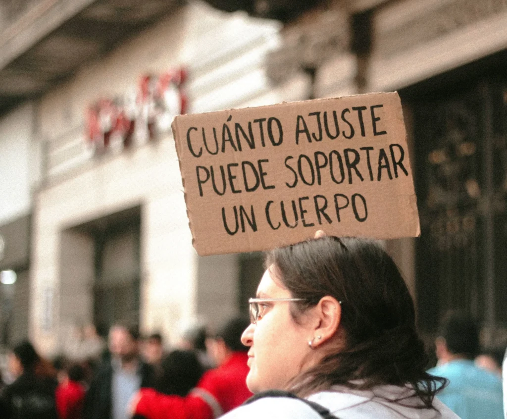 Mulher segura cartaz com a frase “Cuánto ajuste puede soportar un cuerpo” durante protesto, representando o desgaste social causado pela inflação e pelos cortes na Argentina.