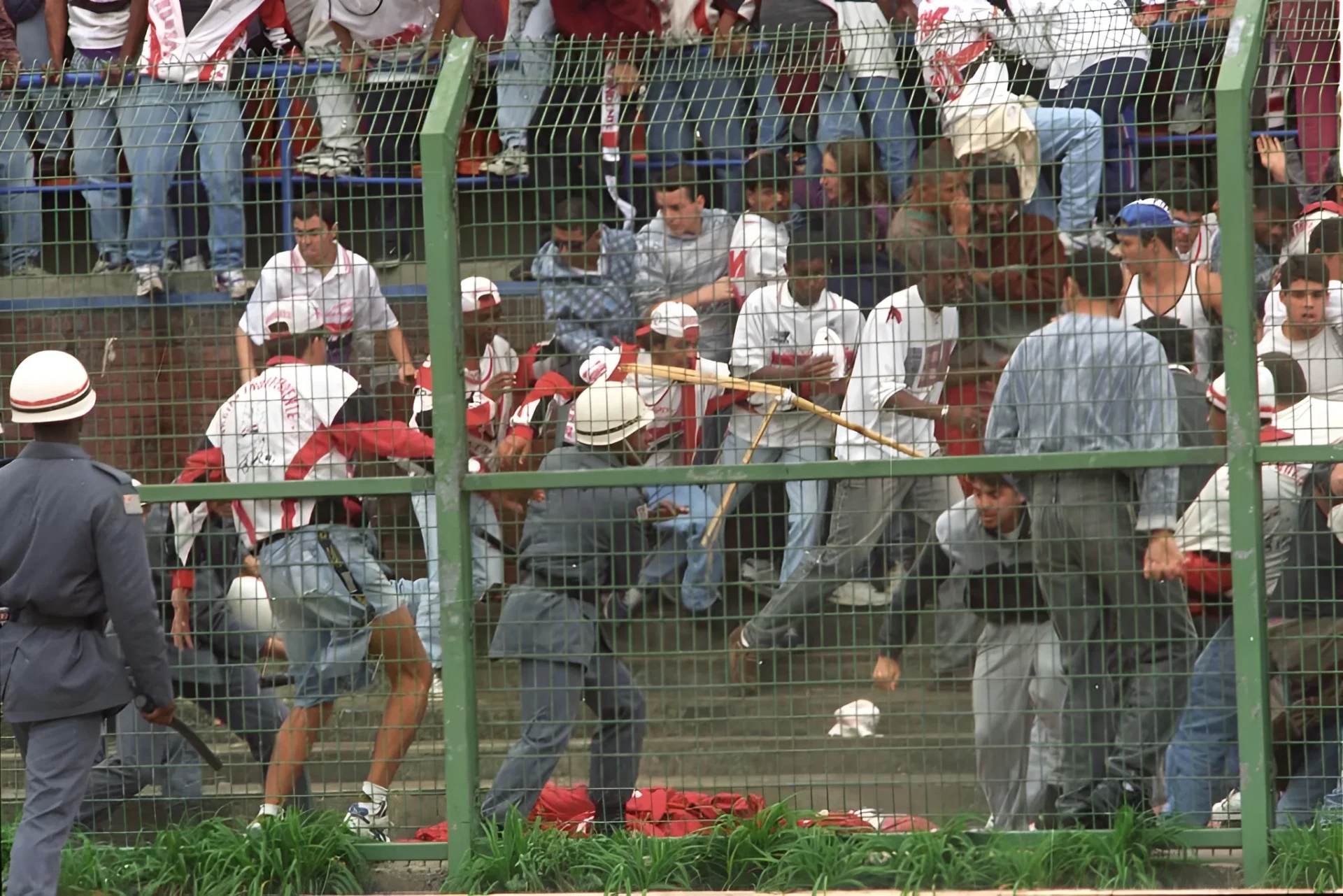 Torcedores em confronto violento em arquibancada cercada por grades no estádio do Pacaembu, ilustrando a repetição histórica da violência no futebol.