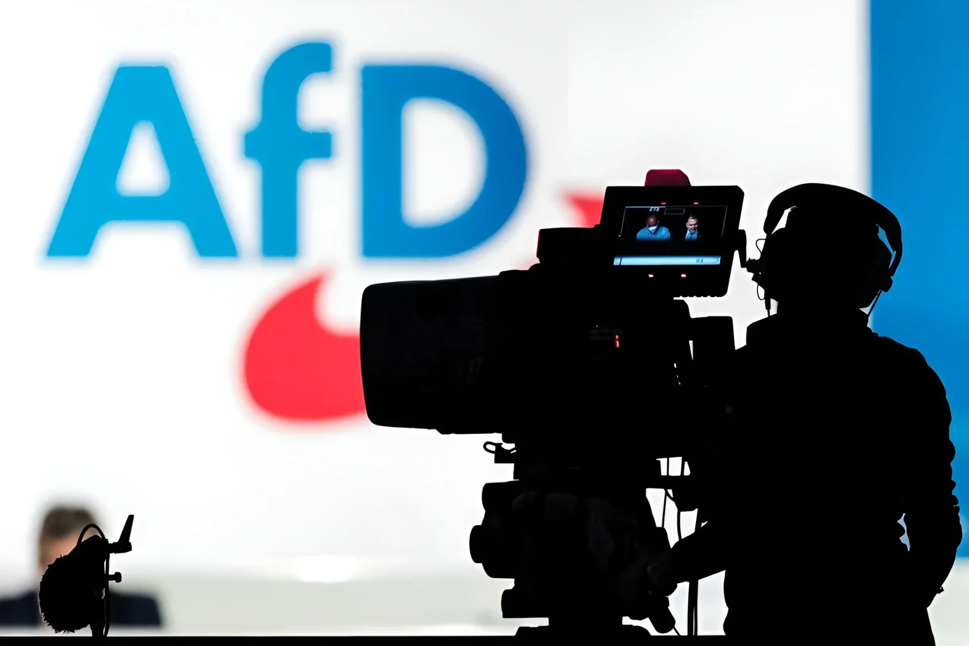 Câmera de televisão aparece diante de painel da AfD em reportagem sobre crescimento da extrema direita entre jovens alemães.