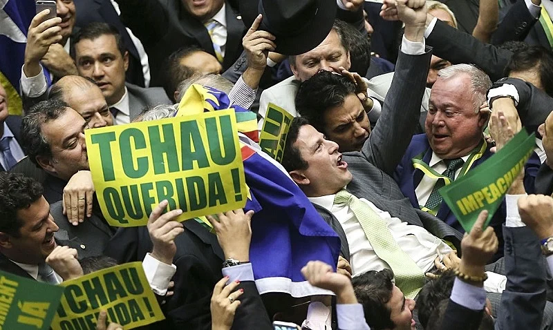 Deputados celebram em plenário a aprovação do impeachment de Dilma Rousseff em 2016, com cartazes 'Tchau Querida' e faixas de apoio ao processo. A imagem documenta o episódio que o artigo analisa como marco fundacional da 'estética do pânico' da extrema direita brasileira — quando a tribuna parlamentar foi usada para evocar terror totalitário em vez de debater bases jurídicas do processo.